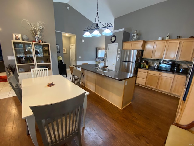 kitchen with a kitchen island with sink, freestanding refrigerator, a sink, light brown cabinetry, and dark countertops