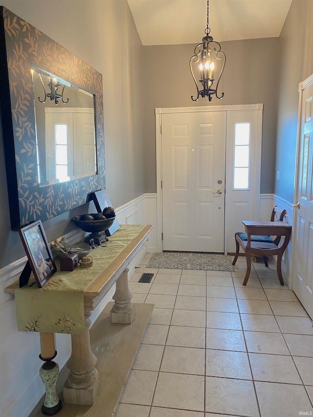 entrance foyer with a chandelier, a wainscoted wall, plenty of natural light, and light tile patterned floors