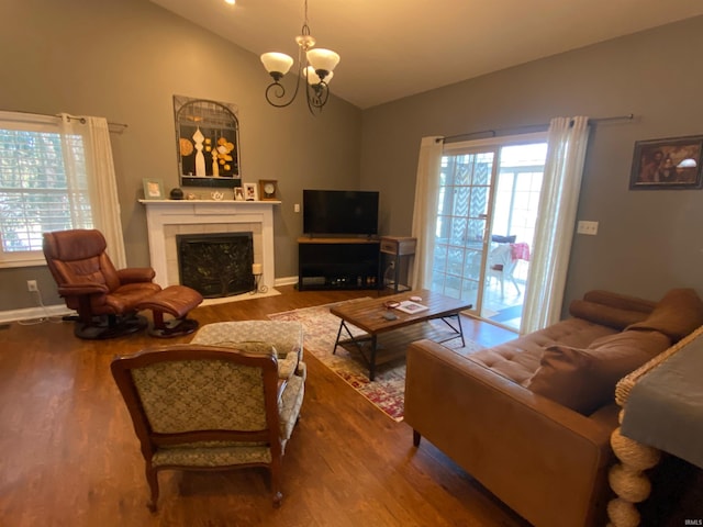 living room featuring wood finished floors, baseboards, lofted ceiling, a tiled fireplace, and a chandelier