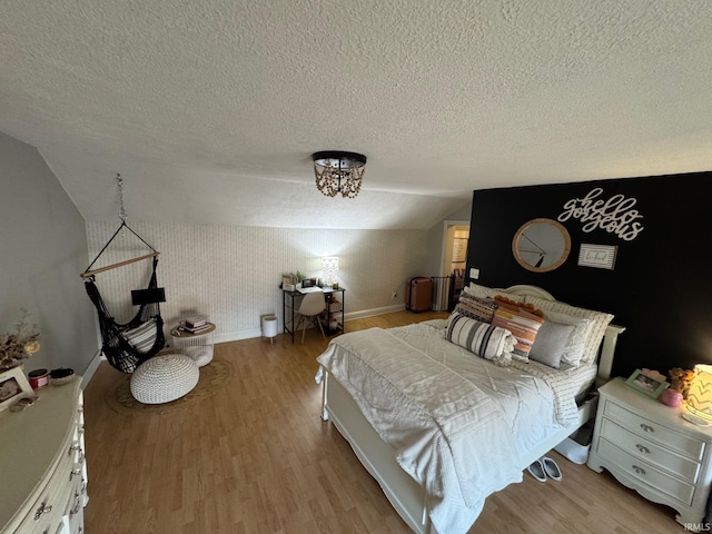 bedroom featuring a textured ceiling, baseboards, light wood-style floors, and vaulted ceiling