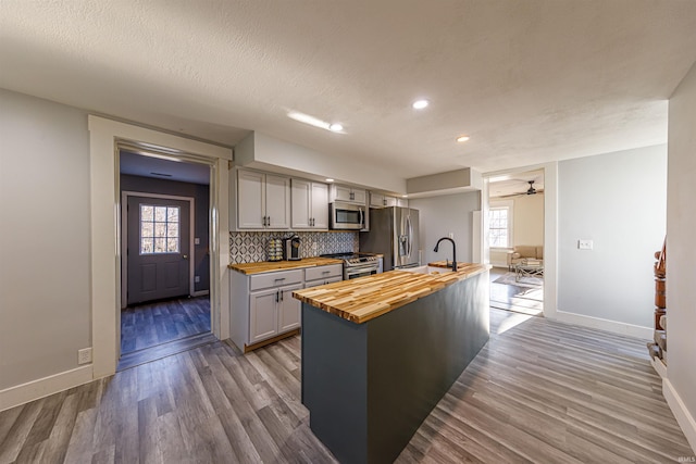 kitchen featuring stainless steel appliances, tasteful backsplash, butcher block countertops, and wood finished floors