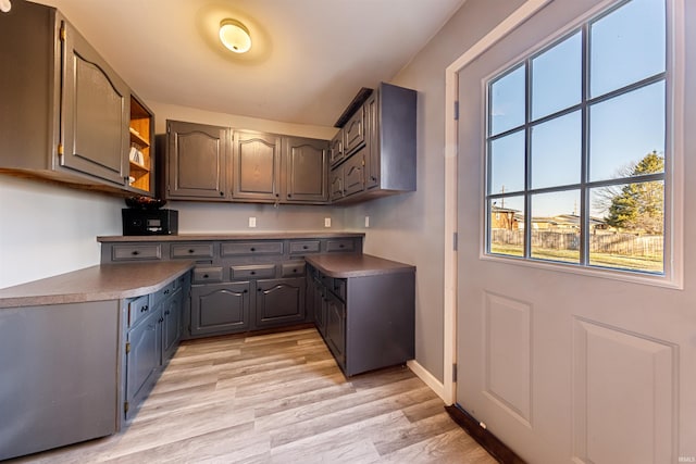 kitchen featuring baseboards, open shelves, gray cabinets, dark countertops, and light wood-type flooring