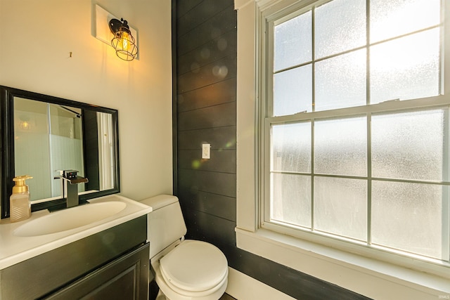 bathroom with vanity, toilet, and wood walls