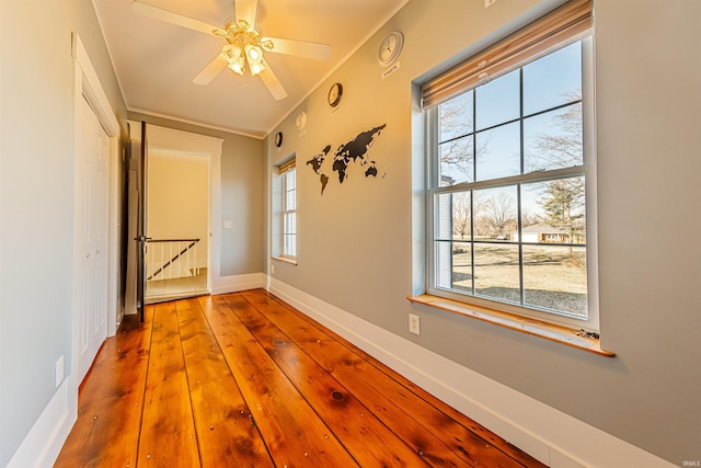 unfurnished room with crown molding, plenty of natural light, wood finished floors, and baseboards