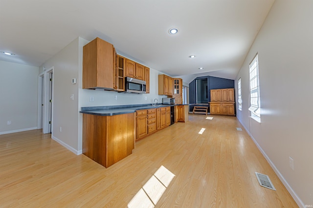 kitchen with dark countertops, brown cabinetry, glass insert cabinets, stainless steel microwave, and light wood-type flooring