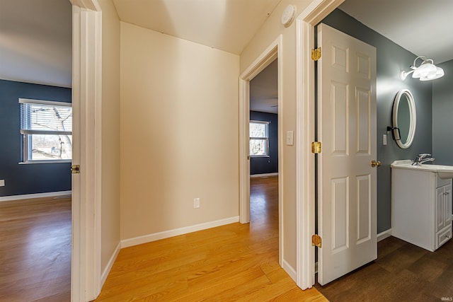 corridor with baseboards, light wood finished floors, and a sink