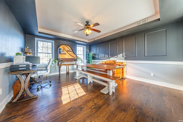 office space featuring wood finished floors, baseboards, visible vents, a tray ceiling, and ceiling fan