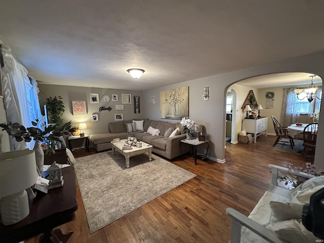 living room featuring baseboards, arched walkways, wood finished floors, and a chandelier