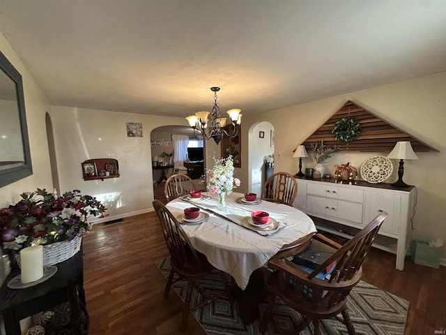 dining area with dark wood finished floors, a notable chandelier, baseboards, and arched walkways