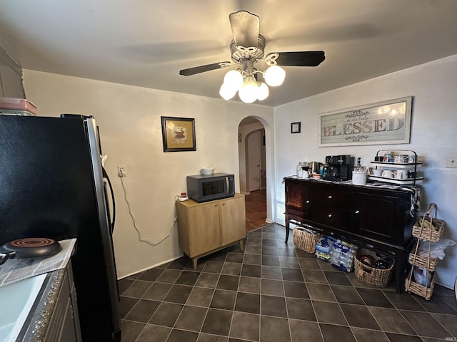 kitchen featuring a ceiling fan, dark tile patterned flooring, arched walkways, freestanding refrigerator, and black microwave