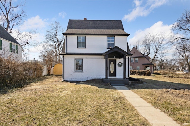 traditional-style house featuring a front yard, brick siding, and a shingled roof