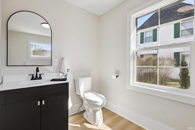 half bathroom featuring toilet, vanity, baseboards, and wood finished floors