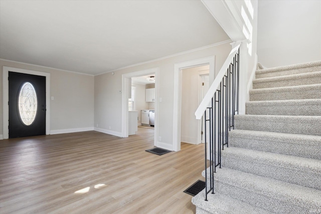 foyer entrance with visible vents, stairway, light wood-style floors, crown molding, and baseboards