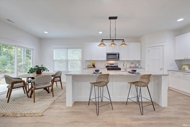 kitchen with backsplash, a center island with sink, light wood-style flooring, appliances with stainless steel finishes, and a kitchen breakfast bar