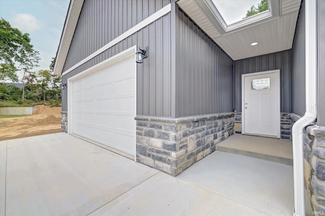 doorway to property featuring a garage, stone siding, board and batten siding, and concrete driveway