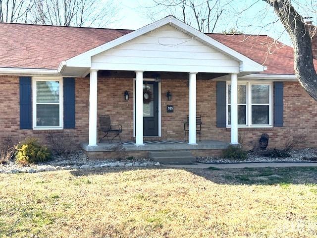 view of front facade featuring brick siding, covered porch, a shingled roof, and a front lawn