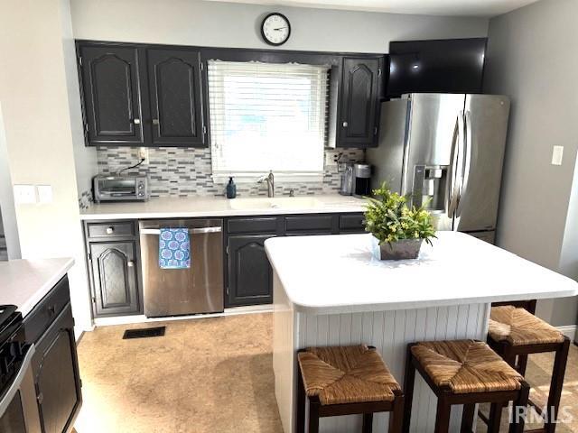 kitchen featuring a sink, stainless steel appliances, a kitchen bar, and backsplash