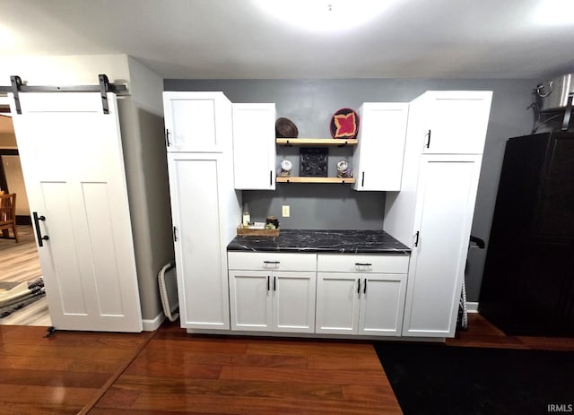 kitchen featuring dark countertops, dark wood finished floors, white cabinets, and a barn door