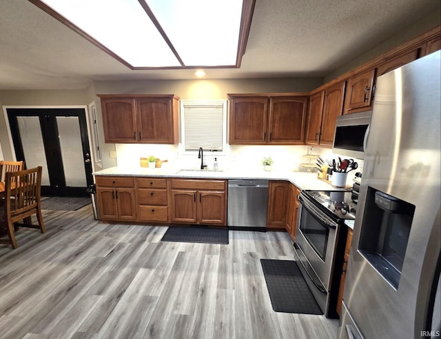 kitchen with light wood-style flooring, a sink, stainless steel appliances, a skylight, and light countertops