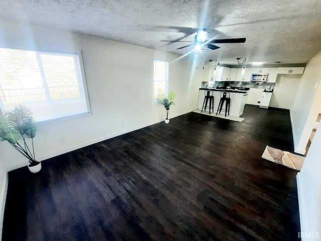 unfurnished living room with baseboards, a textured ceiling, ceiling fan, and dark wood-style flooring