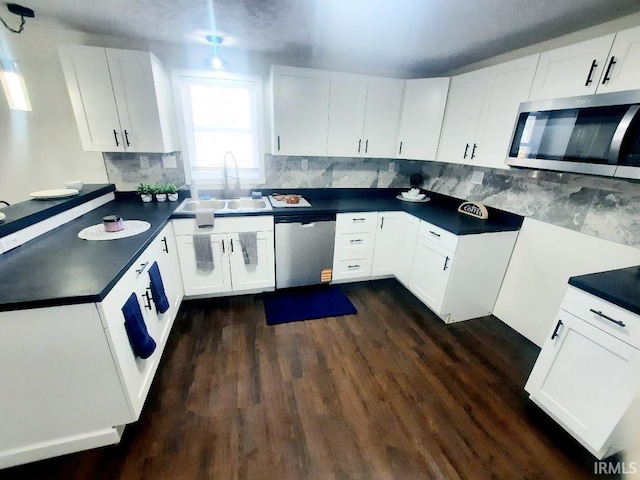 kitchen with a peninsula, a sink, appliances with stainless steel finishes, white cabinetry, and dark countertops