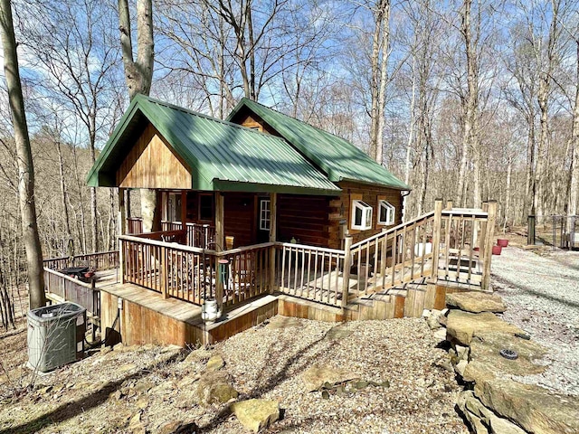 view of front of home featuring a deck, central AC, gravel driveway, metal roof, and log exterior