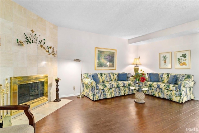 living room with a tiled fireplace, wood finished floors, baseboards, and a textured ceiling