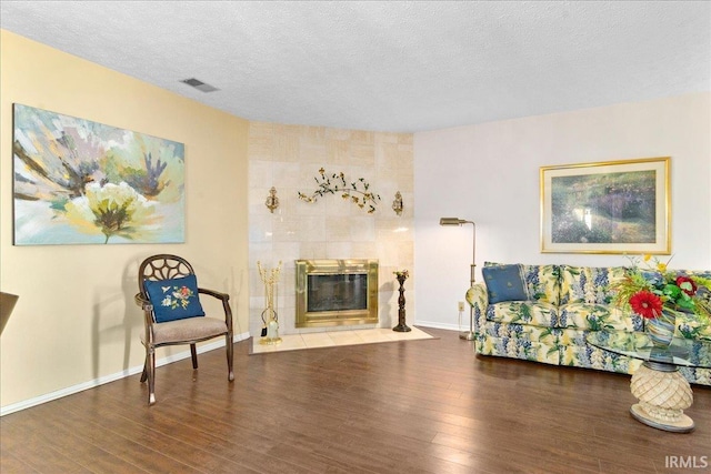 sitting room with visible vents, a tiled fireplace, a textured ceiling, wood finished floors, and baseboards