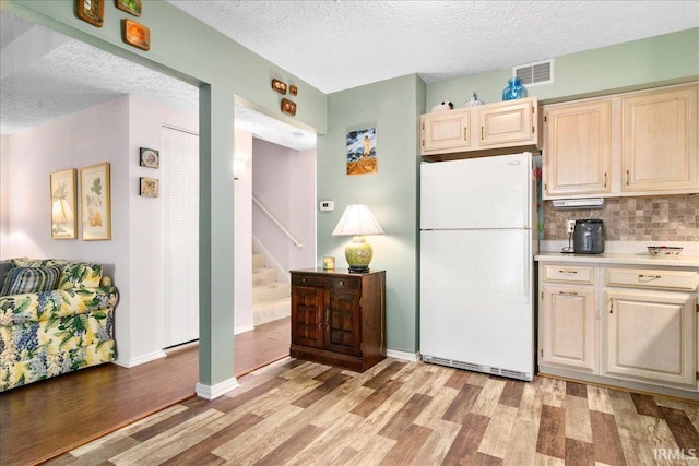 kitchen featuring light wood-style flooring, freestanding refrigerator, decorative backsplash, light countertops, and a textured ceiling