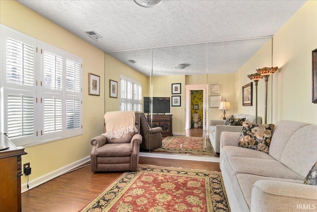 living room featuring baseboards, wood finished floors, visible vents, and a textured ceiling