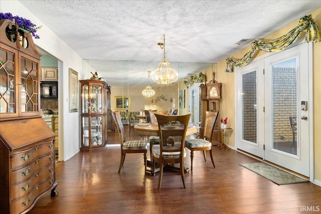 dining area with a notable chandelier, a textured ceiling, visible vents, and dark wood-style flooring