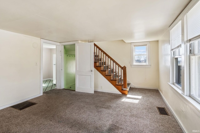 carpeted empty room with visible vents, baseboards, and stairway