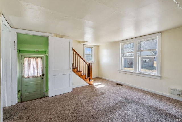 carpeted spare room with visible vents, baseboards, and stairs