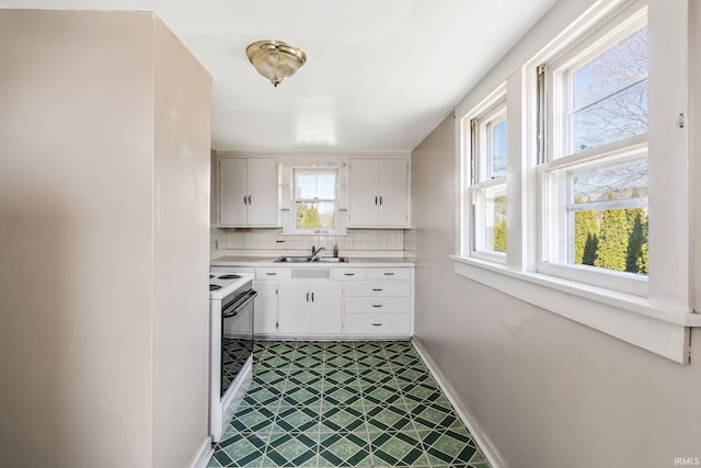 kitchen featuring baseboards, light countertops, decorative backsplash, electric range, and a sink