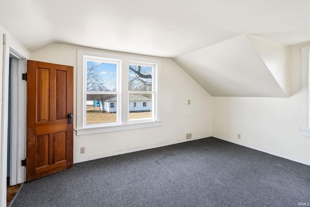 additional living space featuring lofted ceiling, baseboards, and dark colored carpet