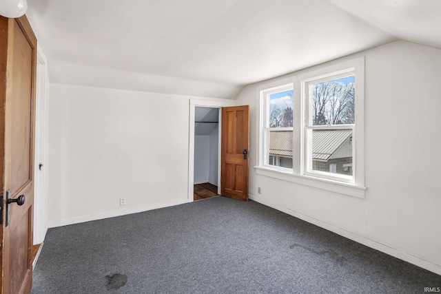 unfurnished bedroom with lofted ceiling, baseboards, a closet, and dark carpet