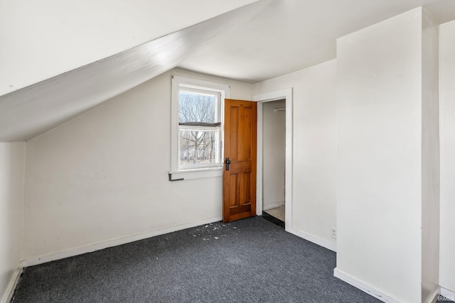 additional living space with baseboards, lofted ceiling, and dark colored carpet