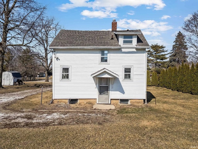 back of property with an outbuilding, a yard, a shingled roof, a chimney, and a storage unit