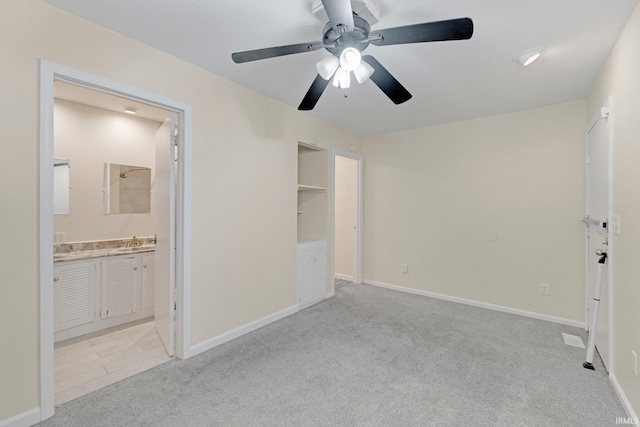 unfurnished bedroom featuring baseboards, light carpet, ensuite bath, a ceiling fan, and a sink