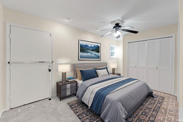 bedroom with visible vents, ceiling fan, light colored carpet, a closet, and a textured ceiling