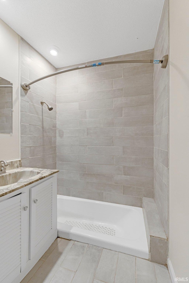 bathroom with tiled shower, a textured ceiling, and vanity