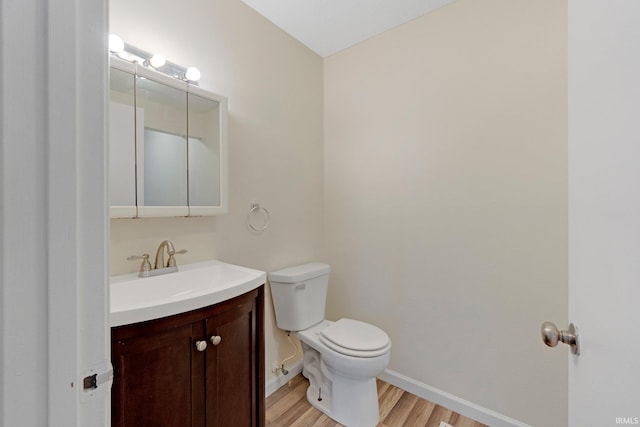 half bath featuring toilet, vanity, baseboards, and wood finished floors