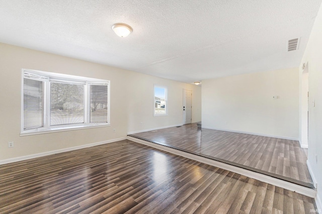 empty room with visible vents, a textured ceiling, baseboards, and wood finished floors