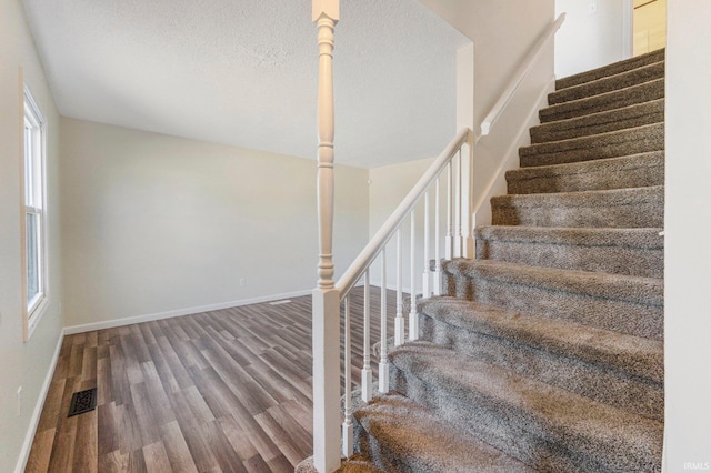 stairs with visible vents, baseboards, a textured ceiling, and wood finished floors