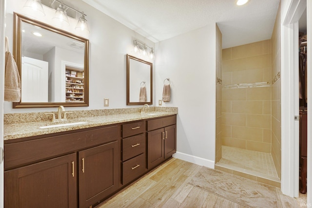 full bath with a sink, wood finished floors, tiled shower, double vanity, and baseboards