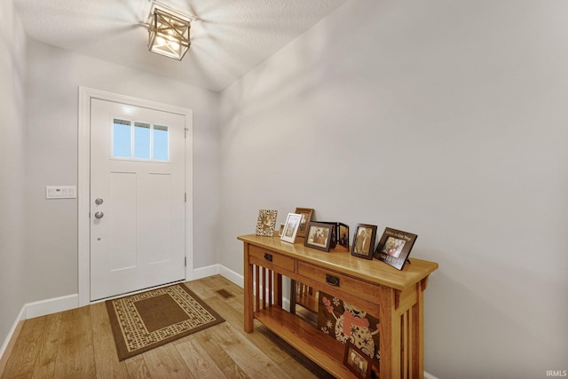 foyer entrance featuring a textured ceiling, baseboards, and wood finished floors