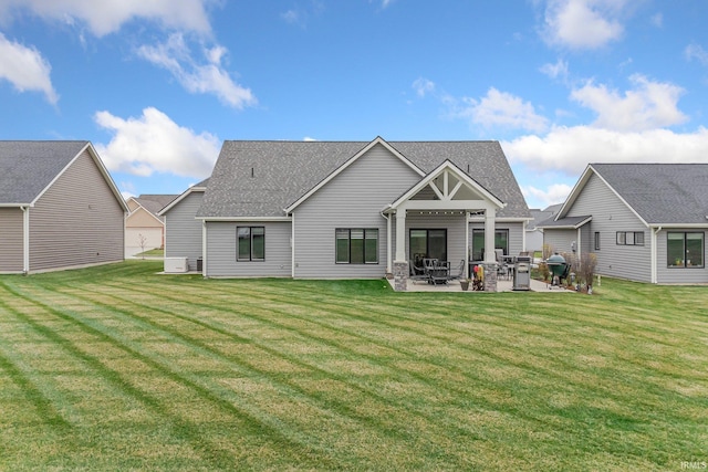 rear view of house featuring a yard, a patio area, and a shingled roof