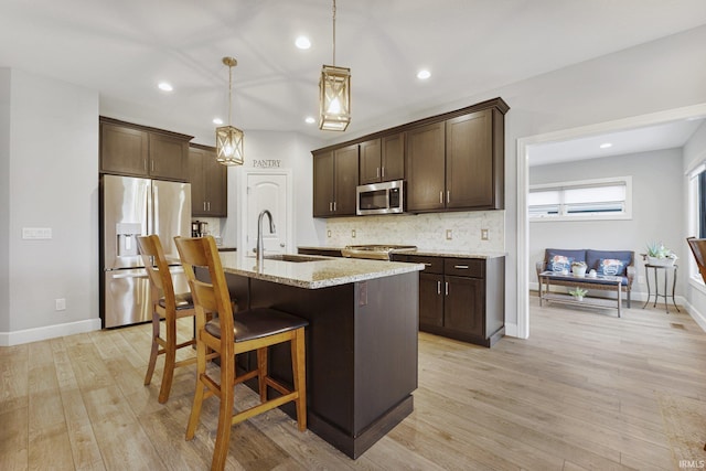 kitchen with a sink, decorative backsplash, dark brown cabinets, appliances with stainless steel finishes, and a kitchen breakfast bar