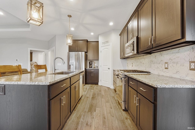 kitchen featuring light stone countertops, decorative backsplash, light wood-style floors, stainless steel appliances, and a sink