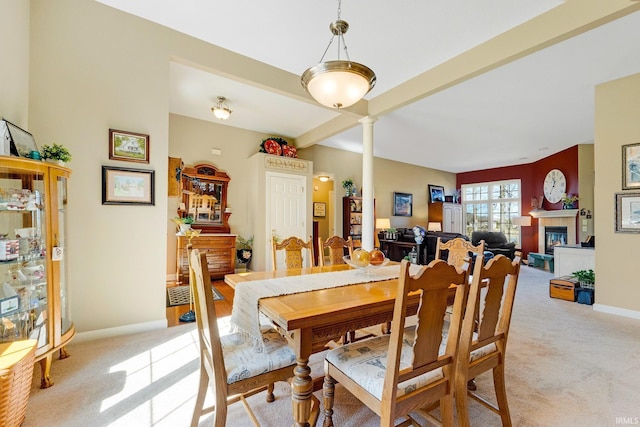 dining area with baseboards, beam ceiling, decorative columns, a tiled fireplace, and light colored carpet